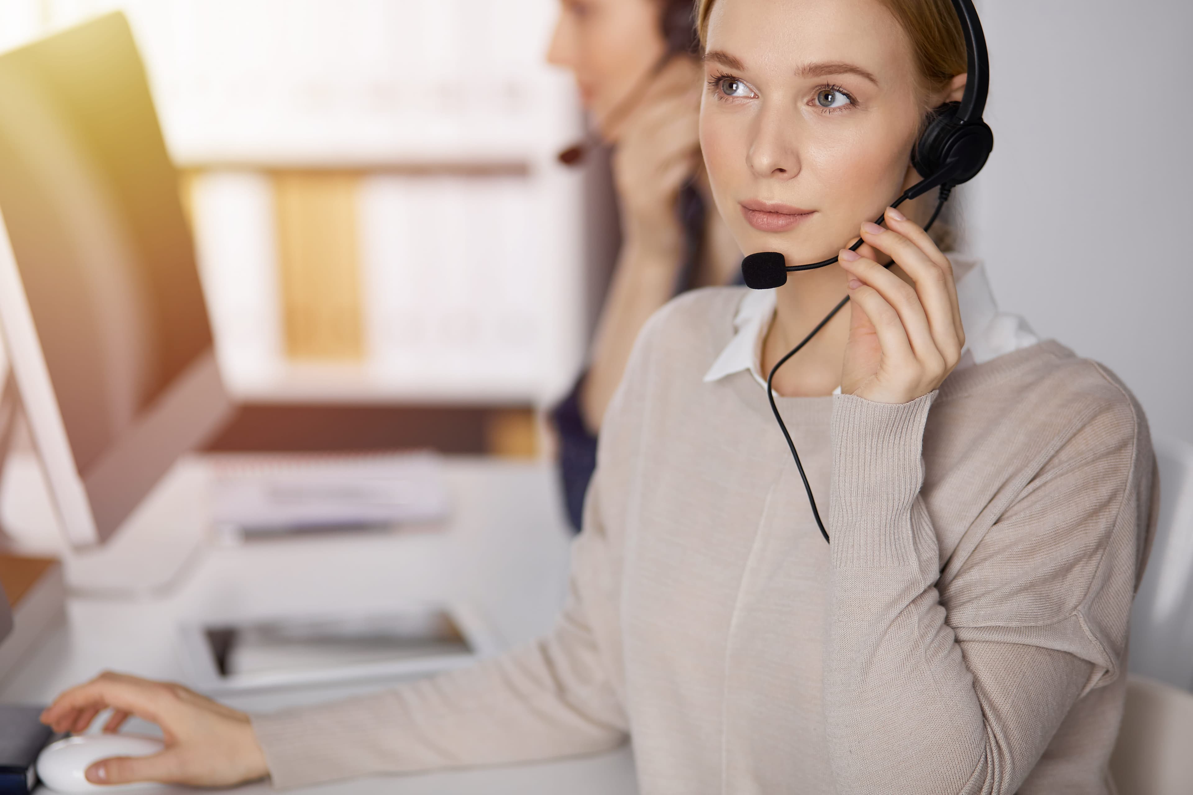 professional female customer support representative smiling warmly at camera, wearing headset and blue corporate attire, sitting at modern office desk, natural lighting, 4k quality